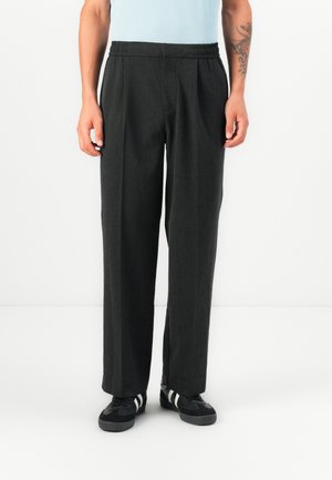 Dark gray trousers with a relaxed fit, elastic waistband, and subtle texture. Paired with black sneakers featuring white stripes.