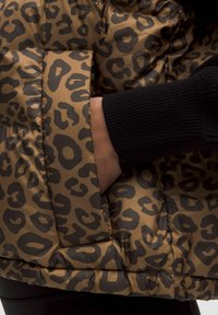 Puffjakke med et brun og sort leopardprint, der har et struktureret stof, ribbede sorte manchetter og en sidelomme.
