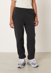 Juodos sportinės kelnės su elastinga juosmens juosta ir šoniniais kišenėmis. Lygi tekstūra, aptemptos prie kulkšnių, su mažo dydžio prekės ženklo logotipu šlaunyje.