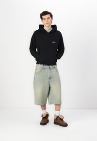 Felpa nera con cappuccio, pantaloni shorts di denim azzurri, stivali alla caviglia marroni con rivestimento beige, abbinati a calzini bianchi. Outfit semplice e casual.