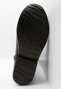 Semelle en caoutchouc noir avec un motif de traction texturé, comportant le texte en relief "MICHAEL KORS" et la taille "7" près du talon.