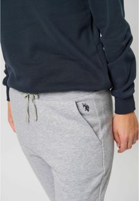 Námornícky sveter s dlhými rukávmi skombinovaný s svetlošedými teplákmi s šnúrkou a malým čiernym logom na vrecku.