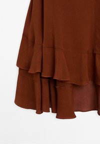 Tissu marron superposé avec des bords froncés montrant la partie inférieure d'un vêtement sur fond blanc.