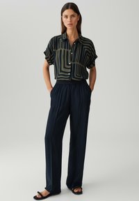 Korte mouwen shirt in donkergroen met abstracte beige lijnen, gecombineerd met marineblauwe wijde broek. Gladde stof en een getailleerde pasvorm met zakken.