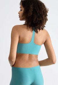 Turkis sports-bh med en glat tekstur, brede stropper og racerback-design, parret med matchende højtaljede leggings.