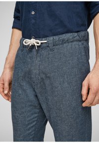 Dark blue džíny s texturovaným povrchem, s páskem na stahování se stříbrnými prvky a uvolněným střihem.