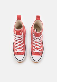 Baskets montantes en toile rouge avec lacets blancs, embout en caoutchouc et accents texturés. L'intérieur est beige, avec un logo sur la semelle intérieure.