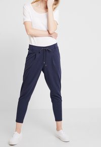 Lättvit t-shirt med korta ärmar; marinblå avslappnade byxor med dragsko midja, avsmalnande ben och framveck; bärs med vita sneakers.