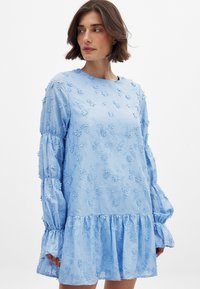 Svetlo modra obleka z cvetličnim vezenjem, dolgimi napihnjenimi rokavi, okroglo ovratnikom in volančastim robom. Narejena iz lahkotnega materiala.