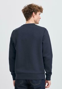 Donkerblauwe sweatshirt met lange mouwen, een ronde hals en een getextureerde stof. Heeft ribgebreide manchetten en een zoom. Eenvoudig, strak design.