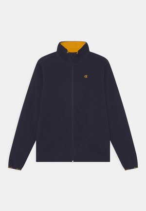 Marineblå fleecejakke med høj krave, gul foring, fuld lynlås og logo på venstre side. Har lange ærmer og elastiske manchetter.