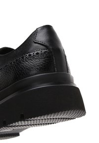 Chaussure en cuir noir avec un dessus texturé, de forme arrondie, et une semelle en caoutchouc épaisse dotée d'un motif de rainure. Agrémentée de détails cousus.