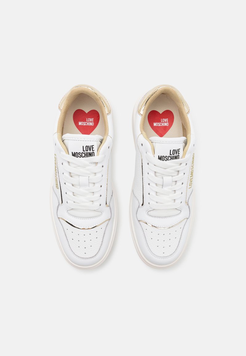 Sneakers bianchi in pelle con dettagli dorati, perforazioni e marchio "LOVE MOSCHINO" sulla linguetta. Soletta a forma di cuore rossa.