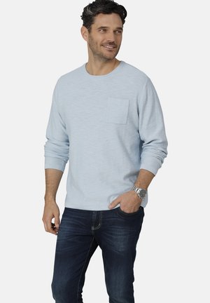 Helles blaues Langarmshirt mit einer Brusttasche, Rundhalsausschnitt, weichem Material, kombiniert mit dunkelblauen Jeans und einer silbernen Uhr.