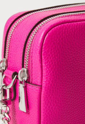 Sac en cuir rose avec une surface texturée, double zip et quincaillerie en ton argent. Comprend une étiquette décorative sur le côté.