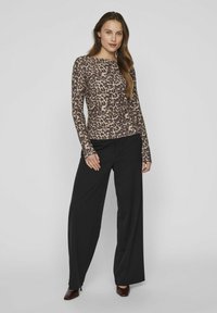 Halenka s leopardím vzorem s dlouhým rukávem v hnědé a černé barvě, kombinovaná se širokými černými kalhotami. Halenka má kulatý výstřih a přiléhavý střih.