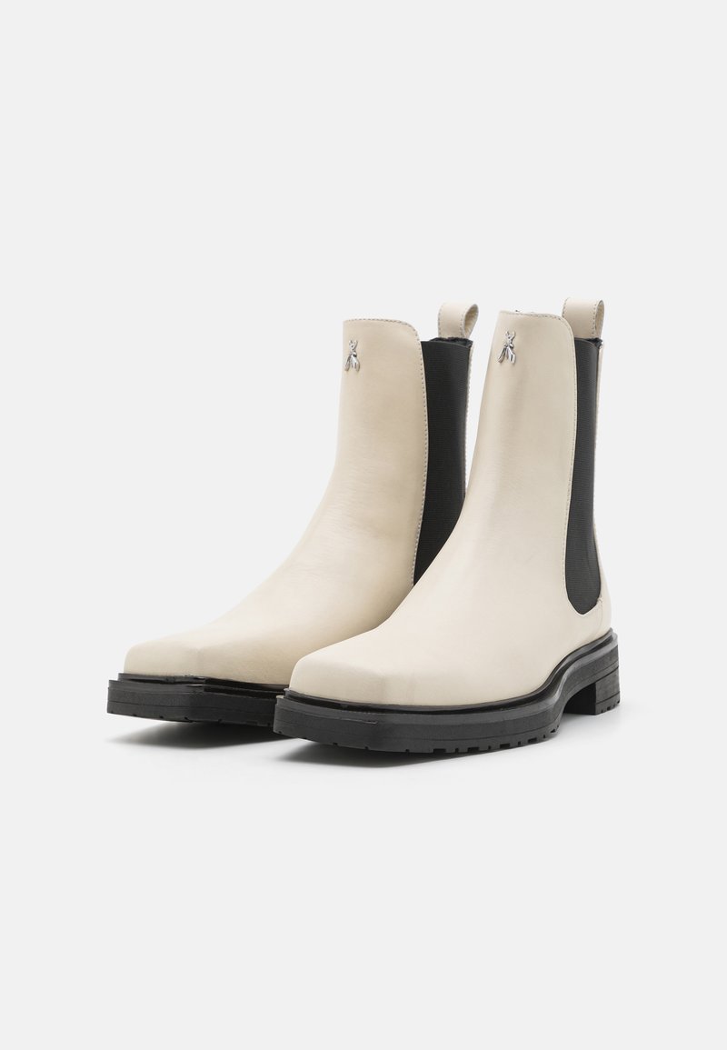 Białe skórzane botki za kostkę z czarnymi elastycznymi panelami bocznymi, okrągłym noskiem i wzorzystą podeszwą. Posiadają metaliczny akcent z logo na cholewce.