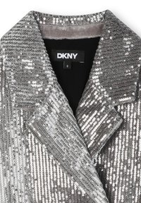 Srebrna marynarka pokryta cekinami z szerokimi klapami i metką marki DKNY wewnątrz kołnierza w czarno-białych kolorach.