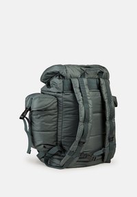 Gepolsterter Rucksack in dunklem Grün mit gestepptem Muster, verstellbaren Trägern, oberem Kordelzugverschluss und seitlichen Taschen. Strapazierfähiges Material.