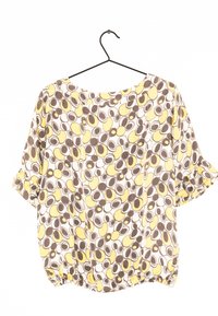 Blouse à manches courtes avec un col rond. Fabriquée en tissu léger, dotée d'un motif circulaire jaune et marron. Ourlet élastiqué.