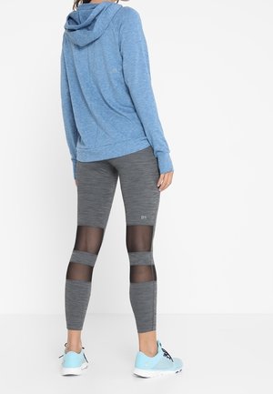 Femme portant un sweat à capuche bleu, des leggings gris avec des panneaux en maille noire à l'arrière des jambes et des baskets bleu clair.