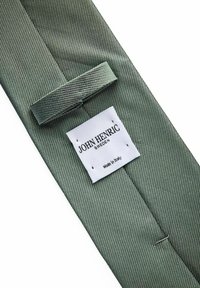 Grön randig silkesfluga med ett texturerat mönster och en vit etikett som läser "John Henric Sweden, Made in Italy." Har en ögla för att hålla flugan på plats.