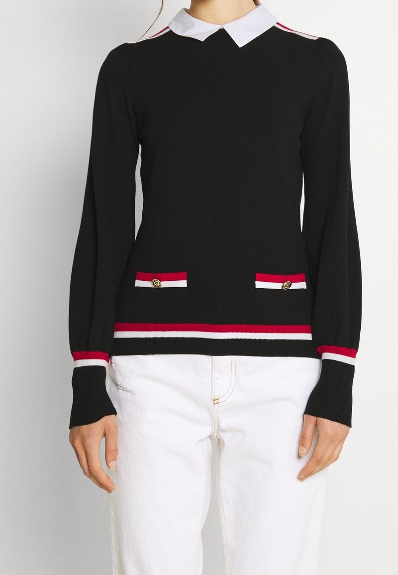 Schwarzer Strickpullover mit weißem Kragen, rot-weiß gestreiften Akzenten an Ärmeln und Saum, mit zwei vorderen Taschen und goldenen Knöpfen.