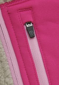 Cerniera fucsia con cursore nero su tessuto lavorato a maglia in diverse sfumature di rosa. Presenta una finitura testurizzata e dettagli di cucitura distintivi.