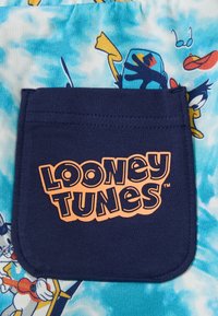 Bolsillo de tela navy con el logo de "Looney Tunes" en naranja, sobre un fondo de color azul claro con efecto tie-dye y ilustraciones de personajes de dibujos animados.