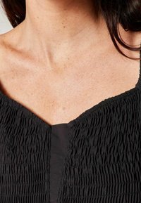 Black top featuring a V-neckline with smocked texture, soft fabric, and a smooth design on the bodice. No visible hardware or patterns.