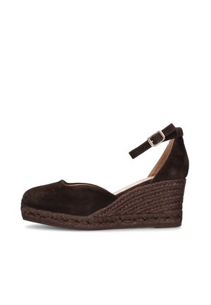 Zapato de cuña de ante marrón con suela de cuerda trenzada y correa en el tobillo con hebilla plateada, visto de lado sobre fondo blanco.