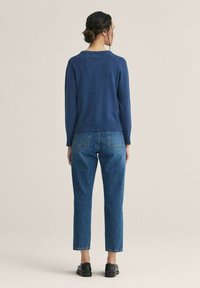 Merinovillapaita, jossa on pyöreä pääntie, yhdistettynä korkeavyötäröisiin vaaleansinisiin farkkuihin ja mustiin kenkiin. Asu näyttää rennolta ja pehmeältä.