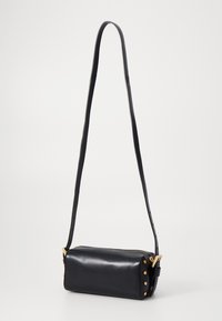Borsa a tracolla in pelle nera con forma cilindrica, dettagli in metallo dorato e chiusura con zip. Presenta una lunga tracolla regolabile.