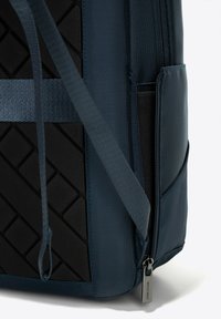 Sac à dos bleu foncé avec un panneau noir texturé, des bretelles ajustables, une poche latérale et un zip avec le nom de la marque.