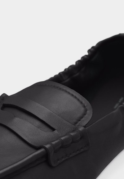 Μαύρο δερμάτινο μοκασίνι με ραφή μοκ-το, ελαστική πίσω πλευρά και διακοσμητικό λουράκι στην πάνω πλευρά.