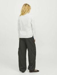 Camisa blanca de manga larga con un cuello estructurado; combinada con pantalones cargo sueltos de color gris oscuro que tienen bolsillos laterales y una silueta relajada.