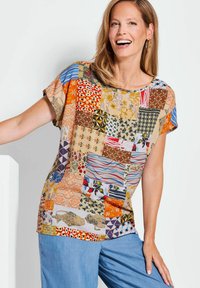 Kurzärmlige Bluse mit einem Patchwork-Design aus verschiedenen Farben und Mustern, überwiegend in Orange, Blau und mit floralen Motiven.
