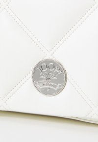 Borsa a tracolla bianca trapuntata in pelle con accento in logo argentato. Presenta cuciture diagonali e una targa metallica rotonda con il nome del brand.