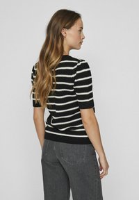 Suéter de punto a rayas en blanco y negro con mangas cortas, dobladillo acanalado y patrón texturizado. Llevado con pantalones de mezclilla grises de talle alto.