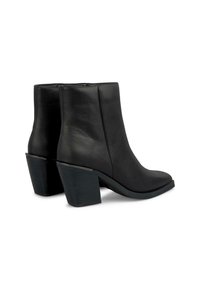 Bottes noires en cuir jusqu'à la cheville avec un bout pointu et un talon épais. Texture lisse, couture minimale et un accent argenté subtil sur le talon.