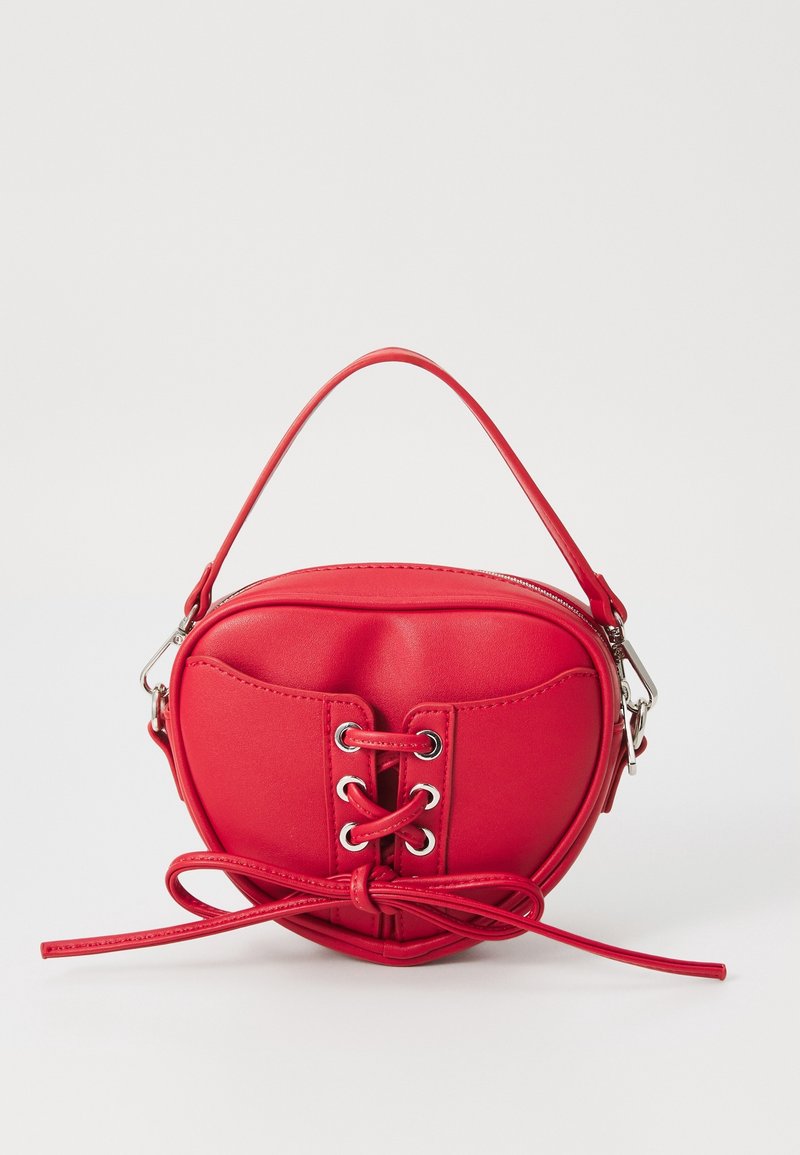 Petit sac à main rouge en forme de cœur avec un détail de laçage devant et une poignée supérieure sur un fond clair uni.