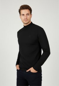 Schwarzes Langarm-Turtleneck-Shirt mit enganliegendem Design, glatter Textur und subtiler Logodetail auf der Brust. Geeignet für Freizeitkleidung.