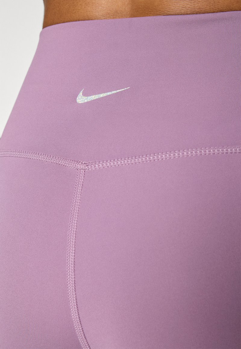 Primer plano de una persona que lleva leggings deportivos de tiro alto en lavanda con un logo reflectante de Nike en la cinturilla.