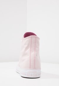 Rosa canvas hög sko med en texturerad yta, vit gummisula och kontrasterande rosa sömmar. Har en logotyp på hälen.