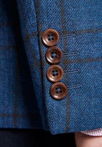 Niebieska marynarka z tkaniny tweedowej z subtelnym wzorem w kratkę, cztery brązowe guziki z krzyżowym wzorem i teksturowane wykończenia.