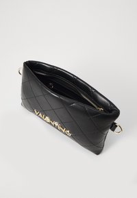 Černá prošívaná kožená kabelka na zip se zlatým logem a bočním kroužkem. Kompaktní obdélníkový tvar, hladký povrch, moderní design.