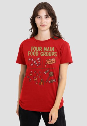 Woman wearing a red T-shirt with "Four Main Food Groups" text and illustrations of candy canes, maple syrup, candy corn, and lollipops.