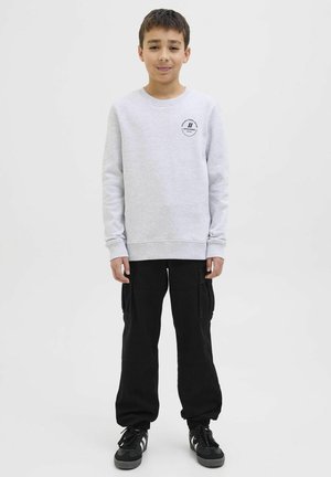Grauer sweatshirt mit langen Ärmeln und rundem Halsausschnitt, mit einem kleinen schwarzen Logo. Kombiniert mit schwarzen Cargo-Hosen und schwarzen Turnschuhen.