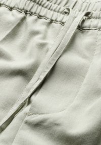 Lichtgroene stoffen shorts met een elastische tailleband, trekkoorddetail en een zijzak. Het materiaal heeft een gladde, textuurachtige afwerking.