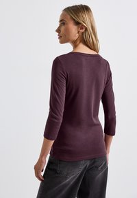 Bordeaux lange mouw top met een ronde halslijn en driekwart mouwen. Zachte textuur, aansluitend design en gladde stiksels aan de onderkant.